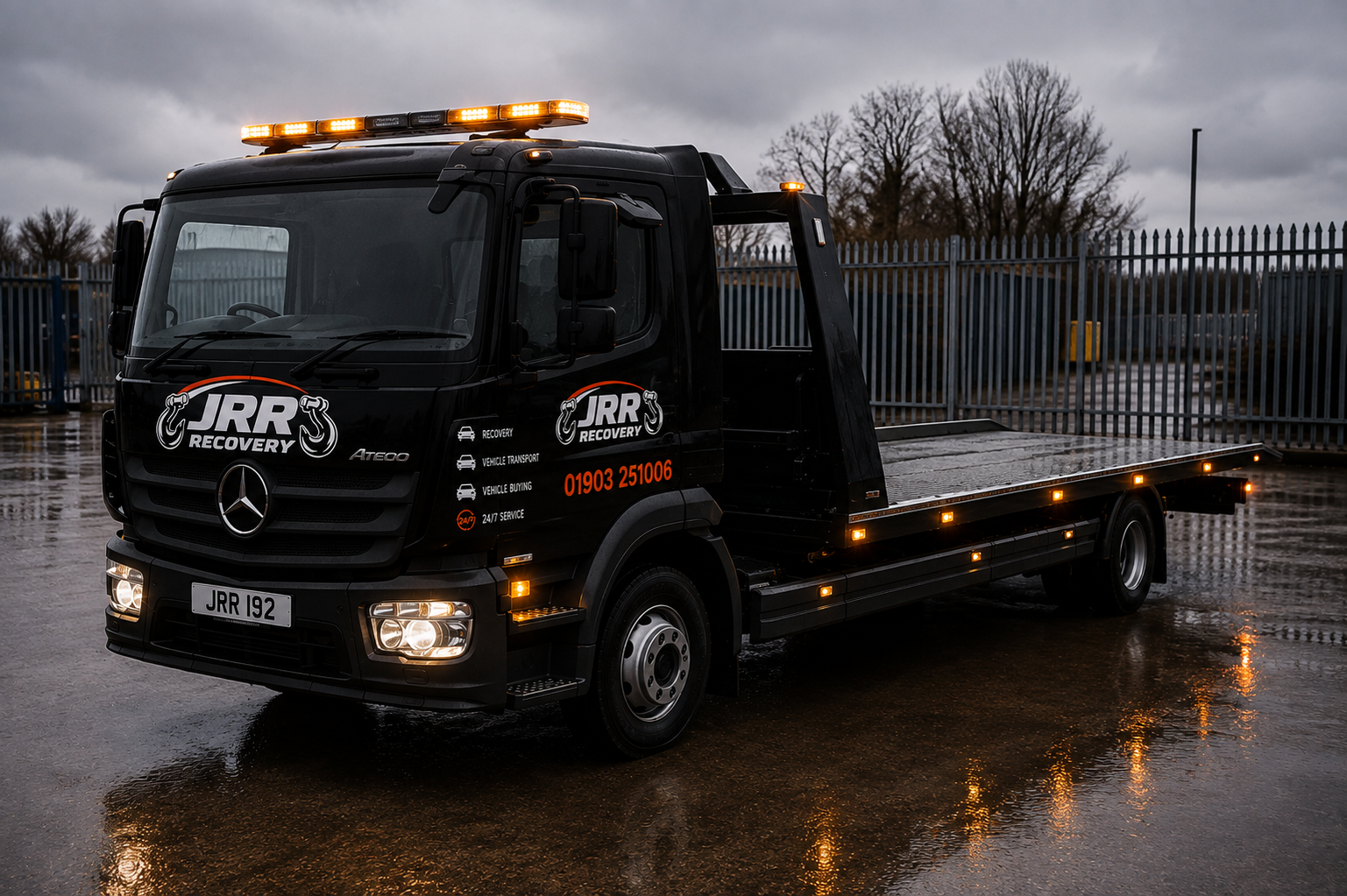 JRR Recovery flatbed truck with amber lights on a wet forecourt